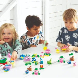 Barn som leker med leklera och formar roliga figurer vid ett bord.